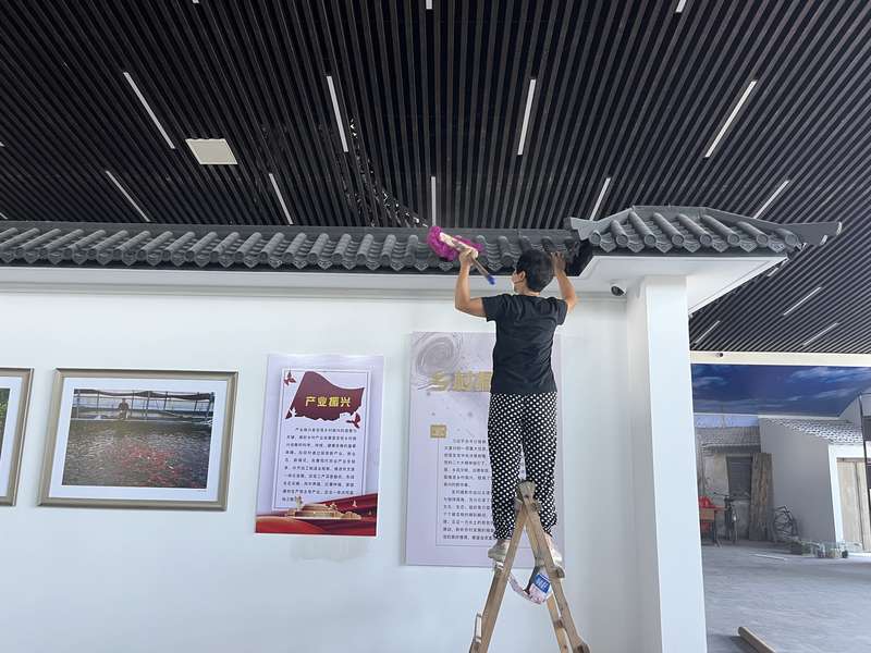 鹿邑某乡村振兴展厅高处清洁,工人擦拭仿古建筑屋檐,产业振兴主题展馆保洁。