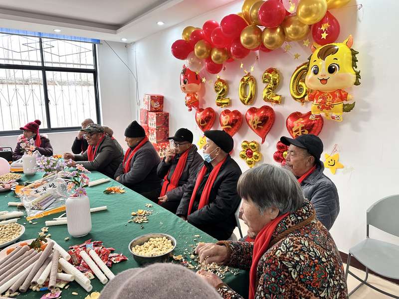 鹿邑社区养老驿站春节联欢活动,老人围坐品尝年货,'2026'气球装饰营造节日氛围。